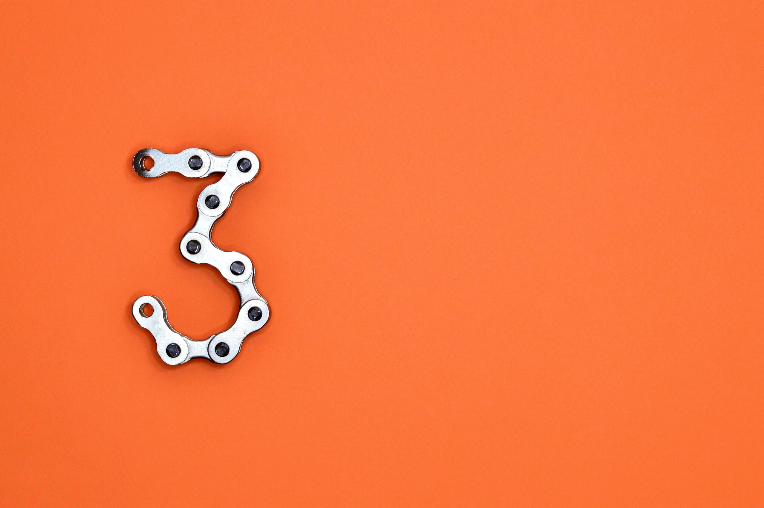 الصفحة الرئيسية A bicycle chain forms the number three against a vibrant orange backdrop, offering ample copyspace.