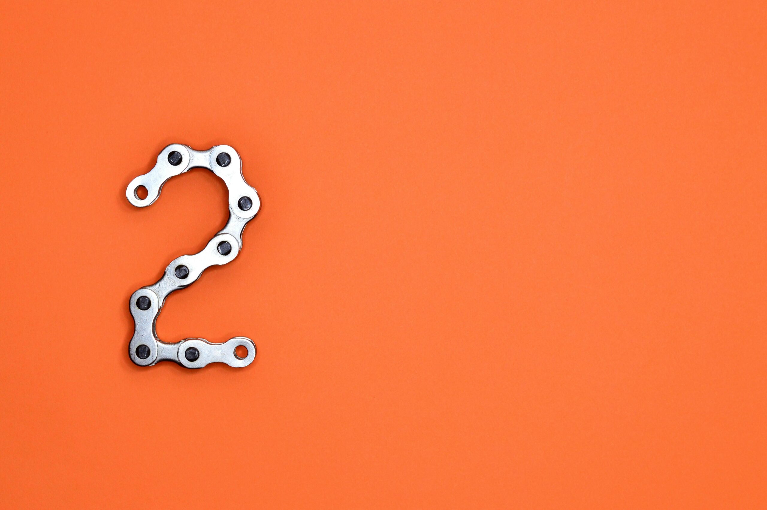 الصفحة الرئيسية Metal chain forming the number 2 on a bright orange background, perfect for design projects.